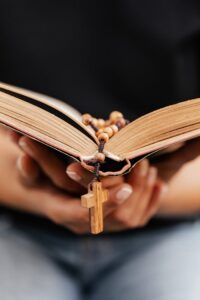 Close-up of hands holding an open Bible with a rosary, symbolizing faith and spirituality.