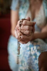 Woman's hands clasped in prayer with a rosary, symbolizing faith and devotion.