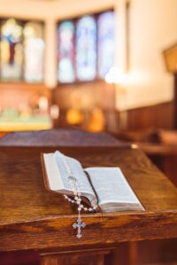 An open Bible with a rosary placed on a wooden altar in a church setting.